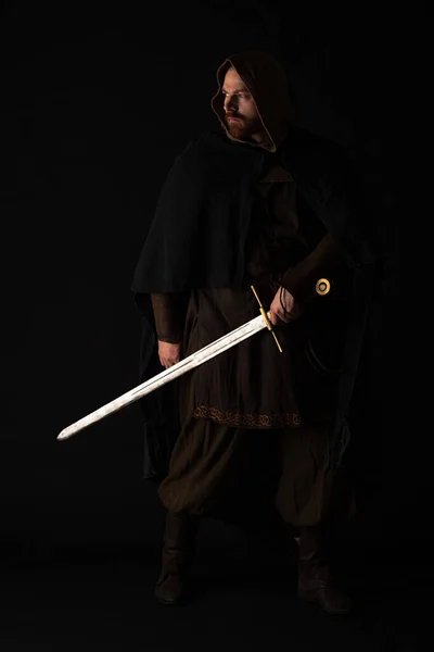 Medieval escocés hombre en mantel con espada en oscuro aislado en negro - foto de stock
