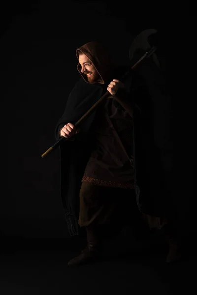 Smiling medieval Scottish warrior with battle axe in mantel isolated on black — Stock Photo