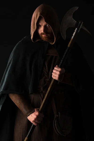 Frowning medieval Scottish warrior with battle axe in mantel isolated on black — Stock Photo