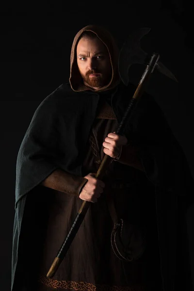 Fruncir el ceño guerrero escocés medieval con hacha de batalla en manto aislado en negro - foto de stock