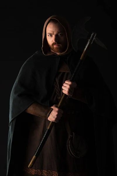 Frowning medieval Scottish warrior with battle axe in mantel isolated on black — Stock Photo