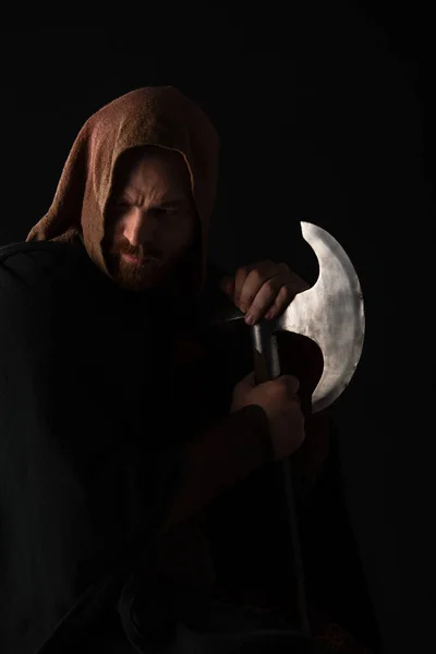 Frowning medieval Scottish warrior with battle axe in mantel isolated on black — Stock Photo