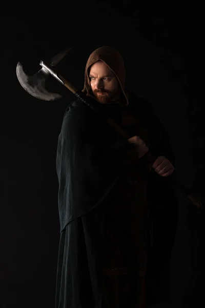 Frowning medieval Scottish warrior with battle axe in mantel isolated on black — Stock Photo