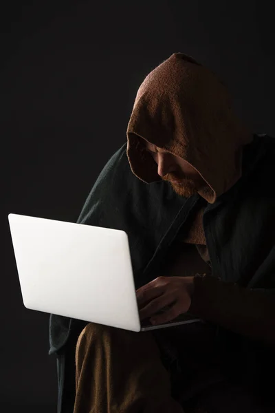 Medieval Scottish man in mantel using laptop in dark isolated on black — Stock Photo