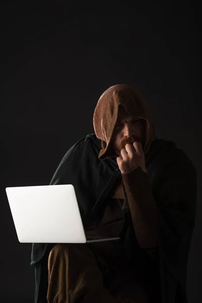 Pensativo medieval escocés hombre en mantel usando portátil en oscuro aislado en negro - foto de stock