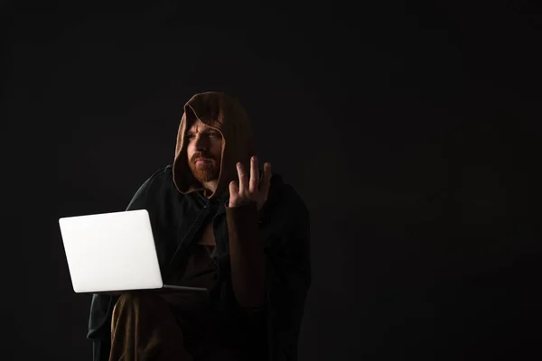Confus médiéval écossais homme dans mantel en utilisant ordinateur portable dans l'obscurité isolé sur noir — Photo de stock
