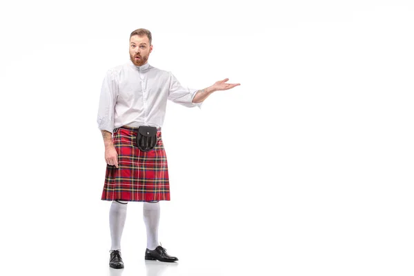 Surprised Scottish redhead bearded man in red tartan kilt pointing with hand on white background — Stock Photo