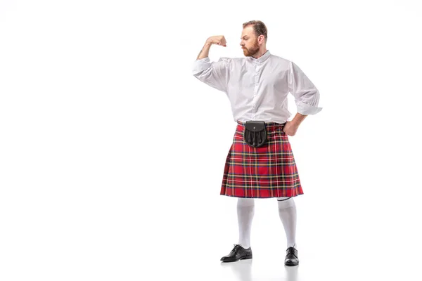 Strong Scottish redhead bearded man in red tartan kilt showing biceps on white background — Stock Photo