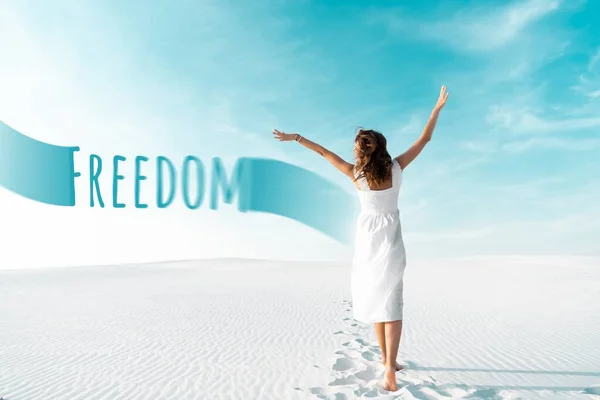 Vista trasera de la hermosa chica en vestido blanco con las manos en el aire en la playa de arena con el cielo azul, ilustración libertad - foto de stock