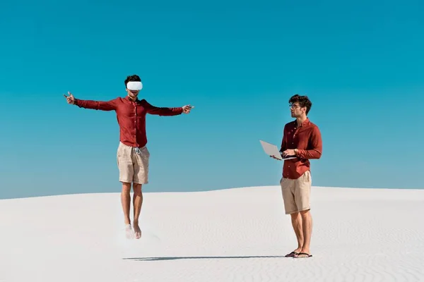 Collage di giovane uomo che salta in cuffia vr e con computer portatile sulla spiaggia sabbiosa — Foto stock