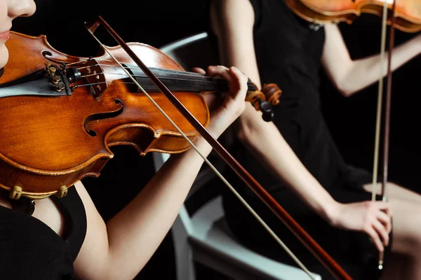 Vista cortada de duas mulheres músicos profissionais tocando em violinos no palco escuro — Fotografia de Stock