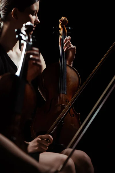 Two professional female musicians playing classical music on violins on dark stage — Stock Photo