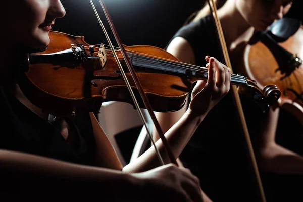 Cropped view of two female professional musicians playing on violins on dark stage — Stock Photo