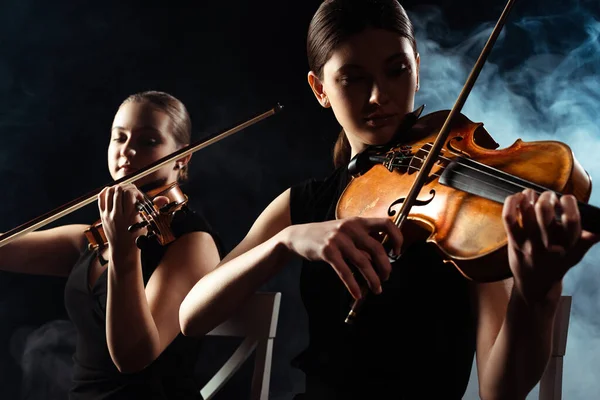 Schöne Musiker spielen auf Geigen auf dunkler Bühne mit Rauch — Stockfoto