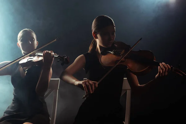 Musikerinnen spielen klassische Musik auf Geigen auf dunkler Bühne mit Rauch — Stockfoto