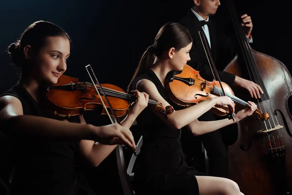 Trío de músicos tocando en contrabajo y violines aislados en negro - foto de stock