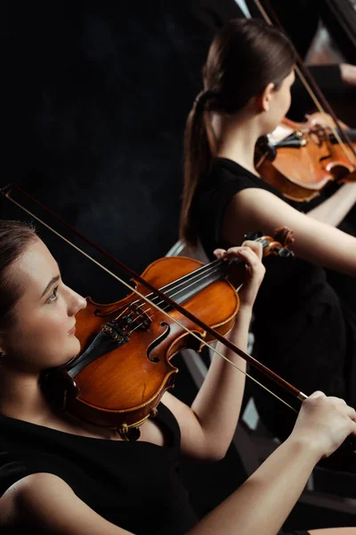 Jóvenes músicos profesionales que tocan música clásica en violines en un escenario oscuro - foto de stock