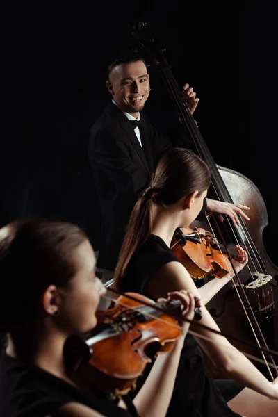 Músicos profesionales felices tocando en contrabajo y violines aislados en negro - foto de stock