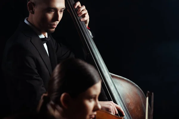 Musiciens professionnels jouant sur violon et contrebasse sur scène sombre — Photo de stock