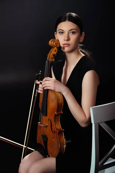 Atractiva músico femenino sosteniendo violín en el escenario oscuro - foto de stock