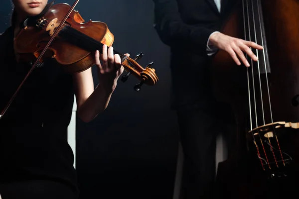 Обрезанный вид профессиональных музыкантов, играющих на скрипке и контрабасе на темной сцене — стоковое фото