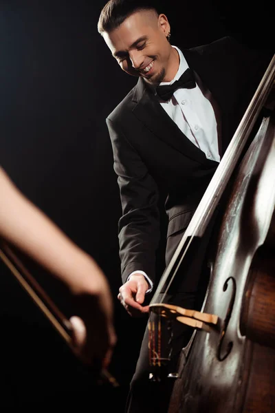 Smiling professional musicians playing on violin and contrabass on dark stage — Stock Photo