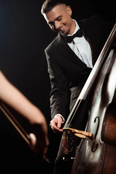 Músicos profesionales sonrientes tocando el violín y contrabajo en el escenario oscuro - foto de stock