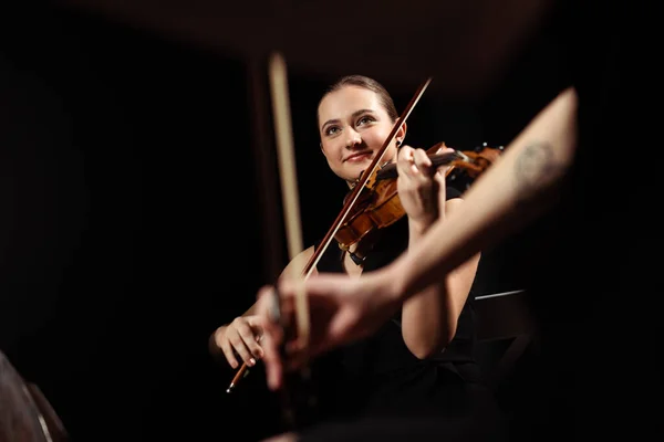 Smiling professional musicians playing classical music on violins on dark stage — Stock Photo