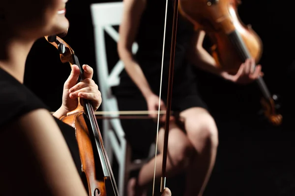 Partial view of female professional musicians playing on violins on dark stage, selective focus — Stock Photo