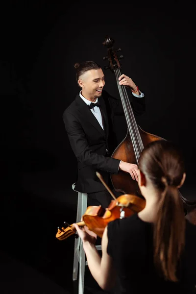 Cheerful professional musicians playing on violin and contrabass on dark stage — Stock Photo