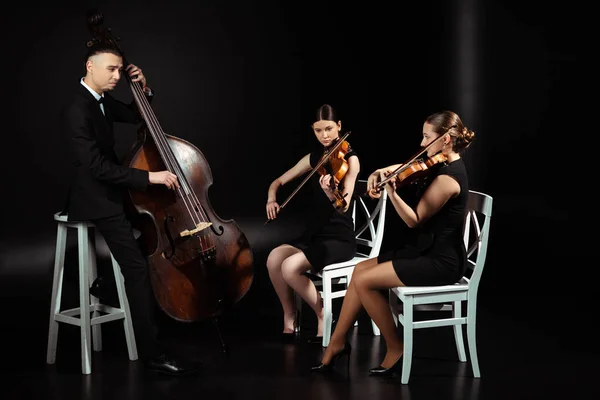 Trio of professional musicians playing classical music on violins and contrabass on dark stage — Stock Photo