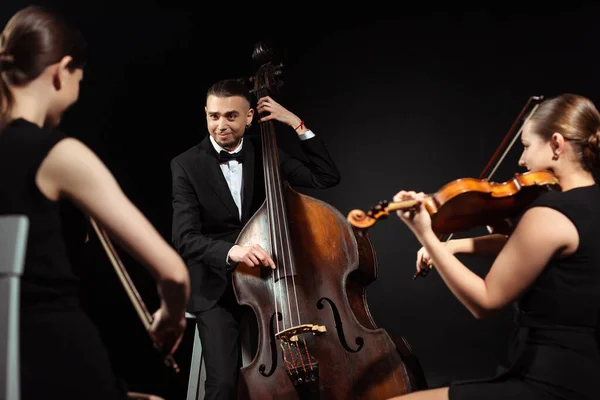 Trio de músicos felizes tocando no contrabaixo e violinos isolados no preto — Fotografia de Stock