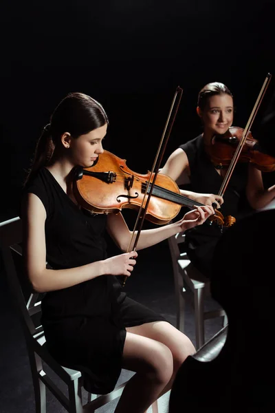 Schöne professionelle Musiker spielen klassische Musik auf Geigen auf dunkler Bühne — Stockfoto