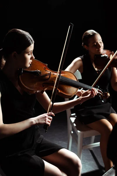 Attraktive professionelle Musikerinnen, die klassische Musik auf Geigen auf dunkler Bühne spielen — Stockfoto