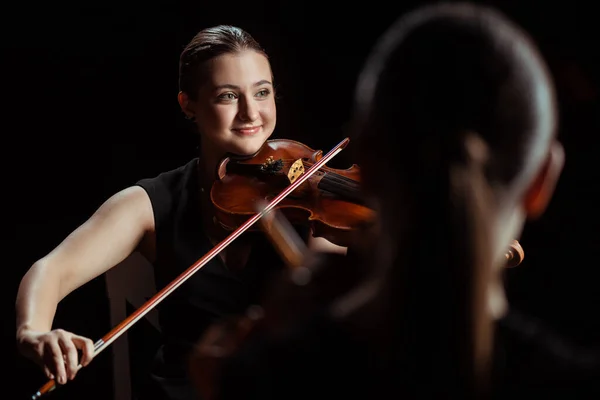 Músicos profesionales felices tocando música clásica en violines en el escenario oscuro - foto de stock