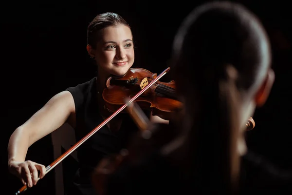Happy professional musicians playing classical music on violins on dark stage — Stock Photo