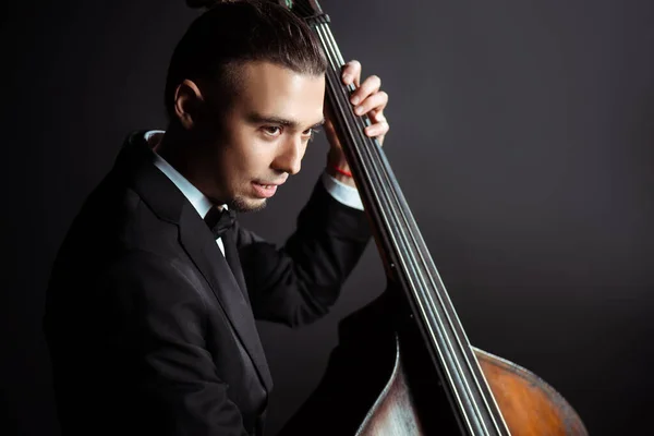 Young professional musician playing on double bass on dark stage — Stock Photo