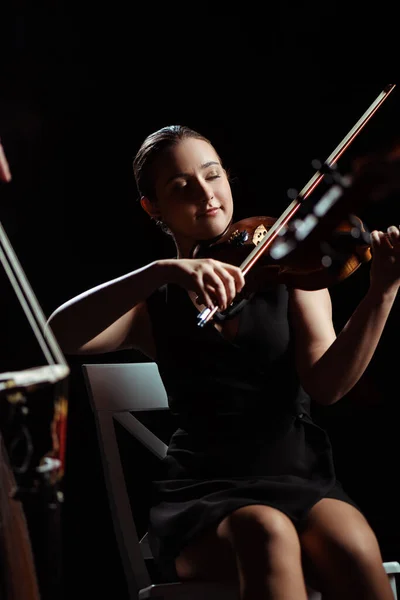 Happy female musician with closed eyes playing on violin on dark stage — Stock Photo