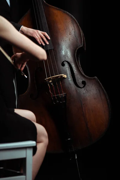 Cropped view of professional musicians playing classical music on violin and contrabass on dark stage — Stock Photo