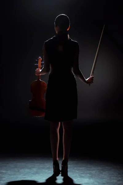 Silhouette of female musician holding violin on dark stage — Stock Photo