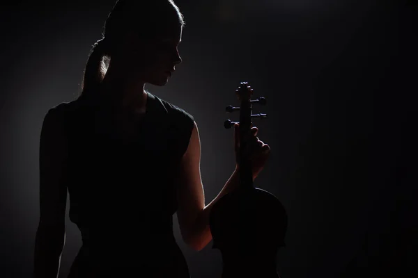 Silueta del músico femenino sosteniendo el violín clásico en el escenario oscuro - foto de stock