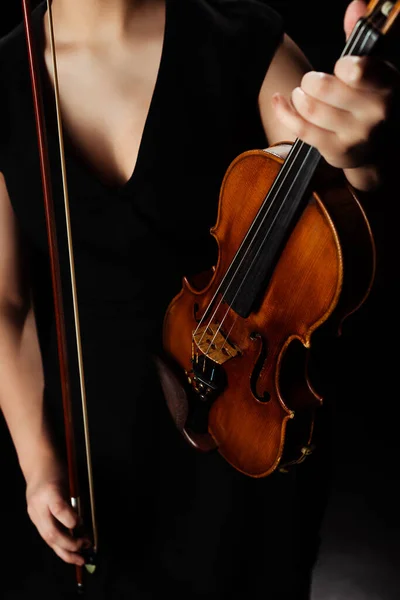 Vista recortada de la música femenina sosteniendo el violín en el escenario oscuro - foto de stock