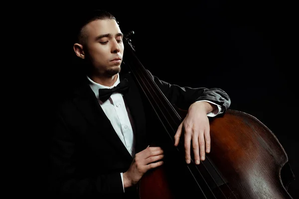 Joven músico tocando en contrabajo aislado en negro - foto de stock