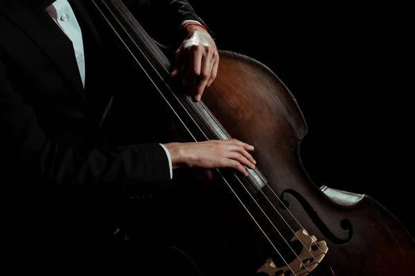 Обрезанный вид профессионального музыканта мужского пола, играющего на контрабасе, изолированном на черном — стоковое фото