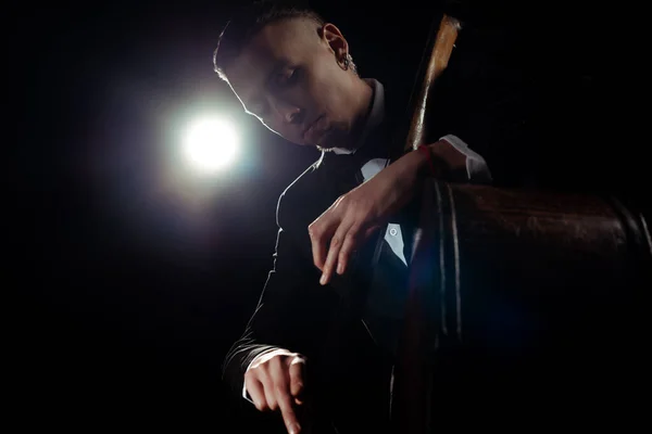 Professional musician playing on double bass on dark stage with back light — Stock Photo