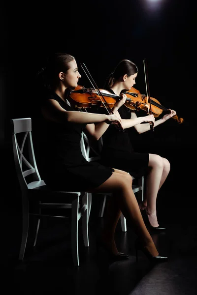 Профессиональные молодые музыканты, играющие классическую музыку на скрипках на темной сцене — стоковое фото
