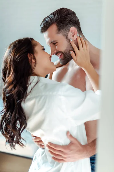 Selective focus of smiling sexy young brunette woman in shirt hugging man with bare torso — Stock Photo