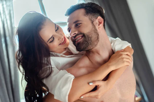 Щаслива сексуальна молода брюнетка в сорочці обіймає чоловіка з голим торсом — стокове фото