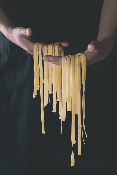 Fresh pasta tagliatelle in man's hands — Stock Photo, Image