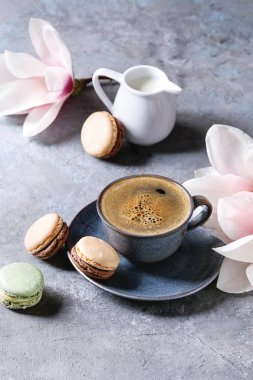 Mavi kupa siyah espresso ile Fransız tatlı macaroons kahve krema ve bahar çiçek Manolya dalları gri doku arka plan üzerinde. Üstten Görünüm, uzay.